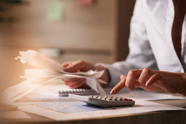 Close up of businesswoman using calculator while going through financial bills. Close up of accountant holding bills and working on calculator in the office. debt stock pictures, royalty-free photos & images