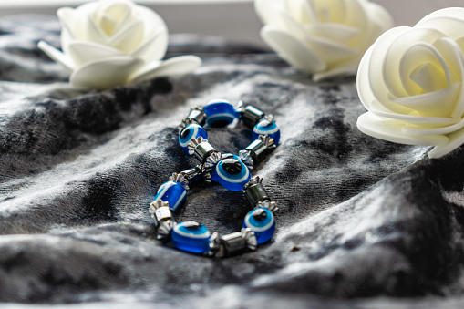 Blue bracelet made of natural stones for women's day, March 8. Figure in the form of eyes and pupil from evil eye, anger and detractors. On grey velvet with white roses.