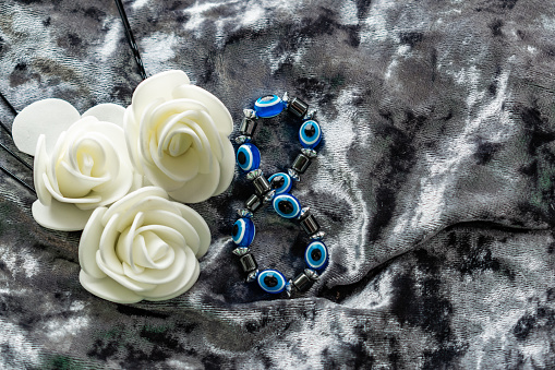 Blue bracelet made of natural stones for women's day, March 8. Figure in the form of eyes and pupil from evil eye, anger and detractors. On grey velvet with white roses.