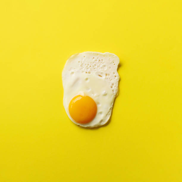 istock One fried egg on yellow paper background. Creative food concept in minimal style. Top view 1147349907