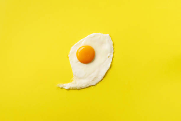 istock One fried egg on yellow paper background. Creative food concept in minimal style. Top view 1147349932