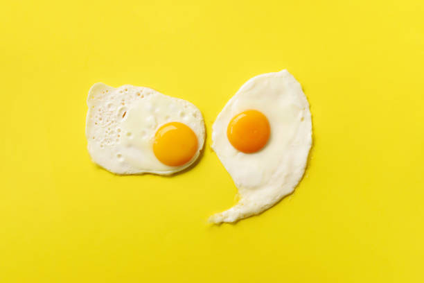 istock Two fried eggs on yellow paper background. Creative food concept in minimal style. Top view 1147349951
