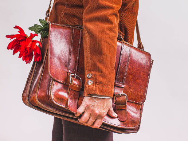 The hand of a man with a business leather briefcase in which a red flower sticks out. A man in a brown corduroy jacket with a leather briefcase in his hand in which a red flower sticks out. uncompromising stock pictures, royalty-free photos & images