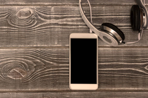 istock Smartphone with black screen, headphones on wooden background. 1147350708