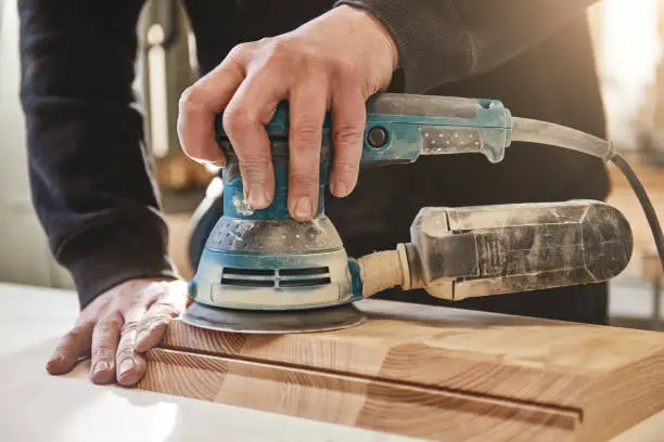 Close up of carpenter polishing wooden board with an orbit sander in the workshop. Horizontal shot