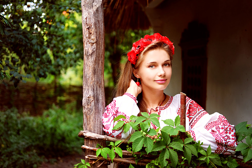 Beautiful slavonic girl with long blond hair and blue eyes with flower crown in white and red embroidered costume.Traditional clothes of Ukrainian region.