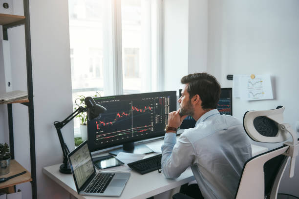 istock Trading on world markets. Young stock market broker analyzing data and graphs on multiple computer screens while sitting in modern office 1147352121