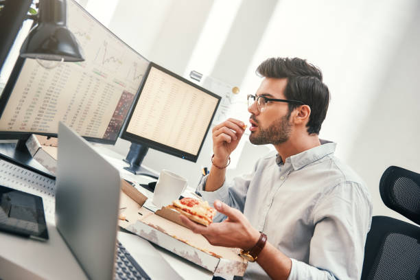 il ne peut pas être la vérité! le jeune commerçant déçu regarde l’écran de moniteur avec des cartes de trading et des données financières tout en mangeant la pizza chaude dans son bureau moderne. - beautiful office people shock photos et images de collection