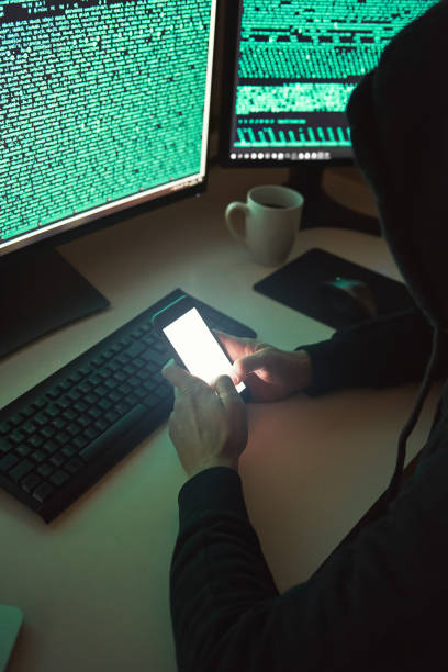 istock Personal information. Vertical photo of young hacker in black hoodie using multiple computers and his smartphone for stealing data while sitting in dark room. 1147352264