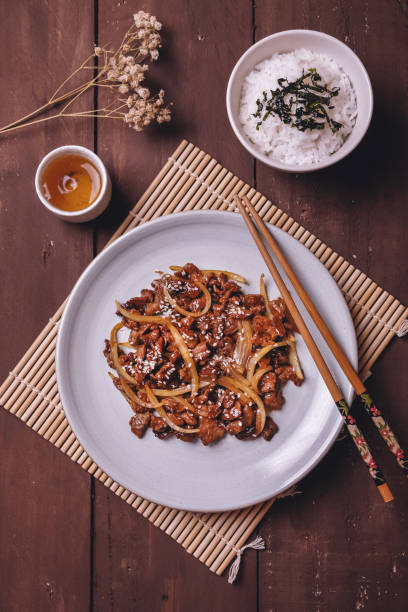 ternera teriyaki con cebolla y sésamo de cerca en un plato sobre mesa de madera - chopsticks stir fried vegetable beef fotografías e imágenes de stock