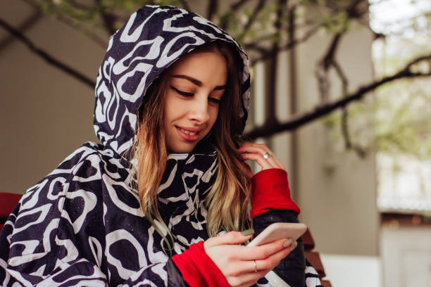 istock Smiling woman in raincoat using mobile phone and texting in social networks, sitting alone 1147358576