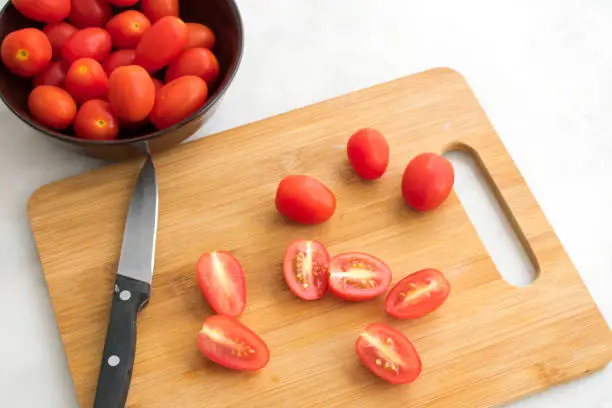 Cutting grape tomatoes in half on a cutting board
