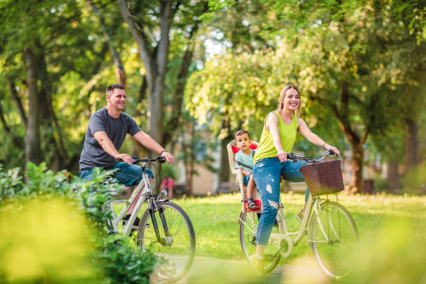 feliz padre y madre con niño en bicicletas divirtiéndose en el parque. - family nature healthy lifestyle happiness fotografías e imágenes de stock