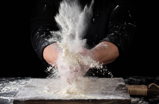 istock chef in black uniform sprinkles white wheat flour over the table 1147374916