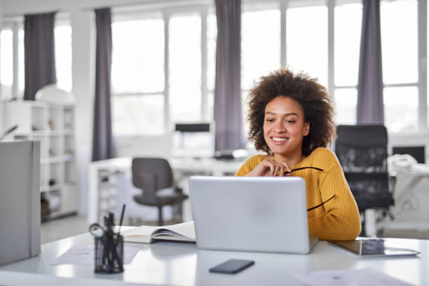 Businesswoman using laptop in office. Beautiful smiling mixed race businesswoman dressed casual sitting in office and using laptop. professional people stock pictures, royalty-free photos & images