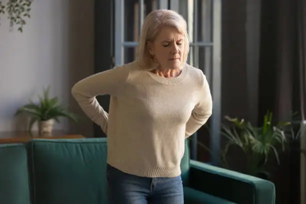 Photo of Unhappy grey haired mature woman touching back, suffering from backache