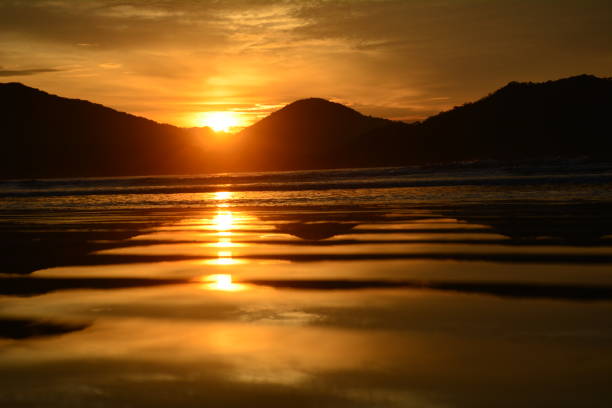 Sun rising on perequê beach in Ubatuba. on the right end of the beach and reflecting on the sea. Scene in orange tones