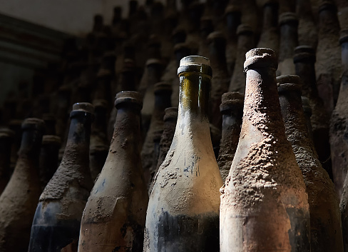 Many aged old bottles with wine and sherry in dark cellar. Dusty and dirty