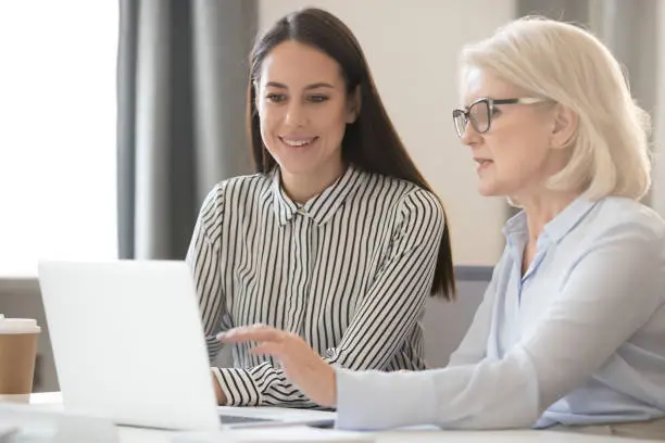 Photo of Confident experienced female employees share information with young worker