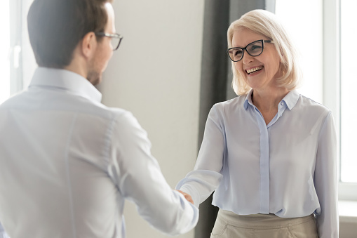 Cheerful middle aged businesswoman handshaking greeting new employee