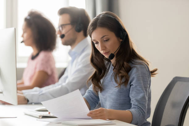 Customer support phone operator sitting at workplace holds read document Telemarketing representative or sales agents sitting at workplace wearing headset use computer, focus on call center member millennial female read document paper, helpline office, busy workday concept complaining stock pictures, royalty-free photos & images