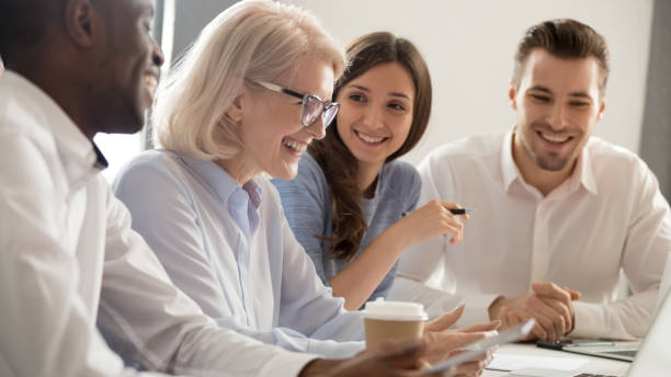 Aged female boss positive staff working together sitting at boardroom