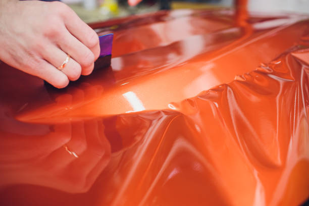 Car wrapping specialist putting vinyl foil or film on car. Selective focus. especialista en envoltorios de automóviles poniendo papel de vinilo o película protectora para envolver el yate, barco, barco, coche, casa móvil. calefacción de película naranja con secador de pelo y recorte suave de plástico de goma de rasqueta