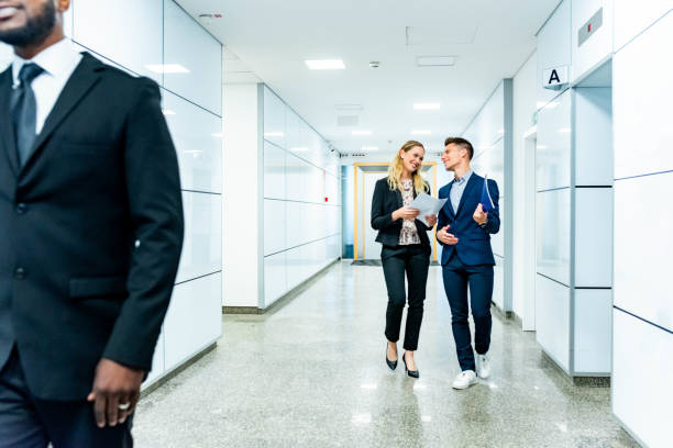 uomini d'affari che camminano in un corridoio di un edificio commerciale - business person vanishing point businessman black and white foto e immagini stock