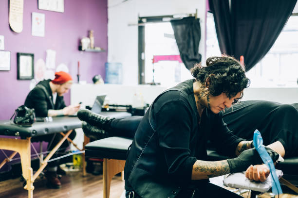 Tattoo artist working in his studio Male tattoo artist tattooing on the arm of the client, in his studio. arm tattoo ideas for men pictures stock pictures, royalty-free photos & images