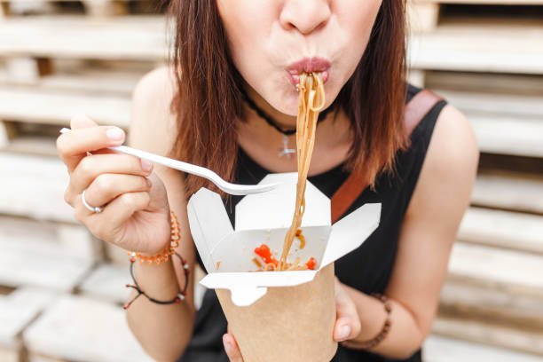 a mulher bonita está comendo o fast food asiático da caixa takeaway. macarronetes deliciosos do wok - places to go - fotografias e filmes do acervo