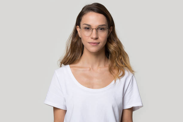 Attractive woman in glasses looking at camera over grey background Head shot portrait caucasian female wearing glasses white t-shirt standing looking at camera studio grey wall background, copy space for ad, eye vision eyesight, selling of optic shop conceptual image beautiful women giving head stock pictures, royalty-free photos & images