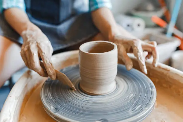 Photo of Top view of hands with clay making of a ceramic pot on the pottery wheel, hobby and leisure with pleasure concept