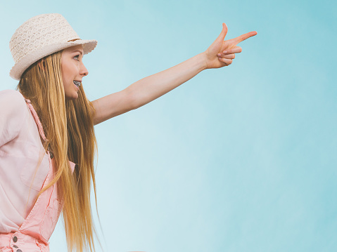 Happy cheerful teenage young woman ready for summer wearing pink outfit and sun hat pointing at copy space