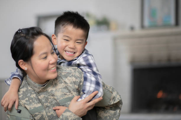 Military Mom Hugging Her Son A mother and her son are hugging in their living room. The mother is wearing a military uniform while they both have a big smile on their faces. filipino family reunion stock pictures, royalty-free photos & images