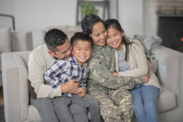 Military Family Sitting On Couch A family of four is happily sitting on the sofa in their living room. The mother has just returned home from serving her country and is wearing a military uniform. filipino family reunion stock pictures, royalty-free photos & images