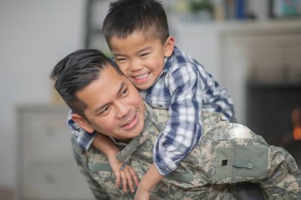 Hugging Dad A military dad and his son are hugging in their living room. The son is smiling happily at the camera. filipino family reunion stock pictures, royalty-free photos & images