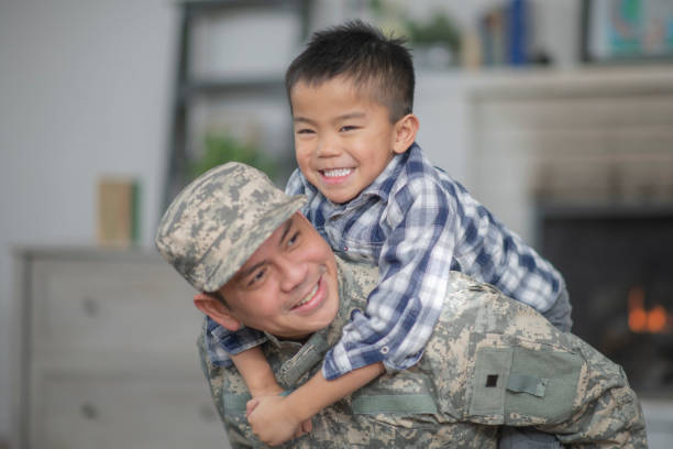 Hugging Dad A military dad and his son are hugging in their living room. The son is smiling happily at the camera. filipino family reunion stock pictures, royalty-free photos & images