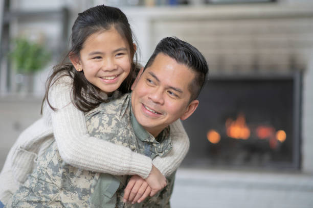 Military Dad Hugging His Young Daughter A father and young daughter are embracing in their living room. The dad is wearing a military uniform and has just returned home. filipino family reunion stock pictures, royalty-free photos & images
