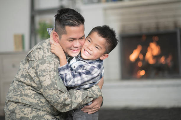 Welcoming Dad Home A military dad and his son are hugging in their living room. The son is running up to the father and jumping into his arms while smiling. filipino family reunion stock pictures, royalty-free photos & images