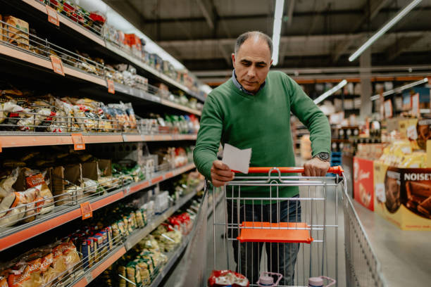 mann mit einkaufsliste kauft lebensmittel im supermarkt - einkaufszettel stock-fotos und bilder