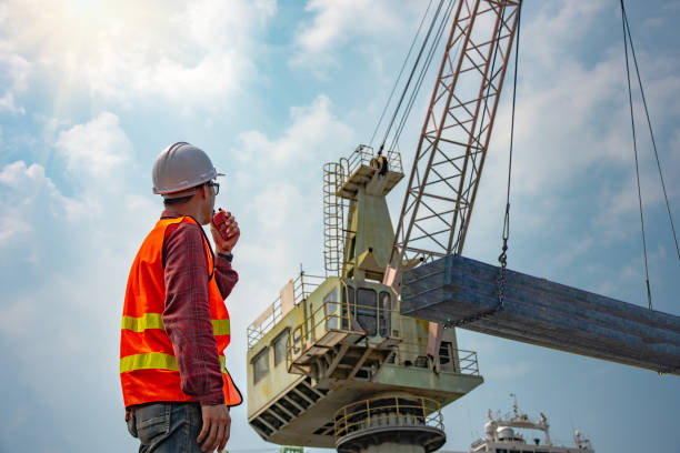 Loading at risk worker stevedore or foreman, engineering, loading master talks to crane driver by walkie talkie for safety lifting the goods shipment, lifting by gantry crane, working at risk on the high level insurance gantry crane stock pictures, royalty-free photos & images