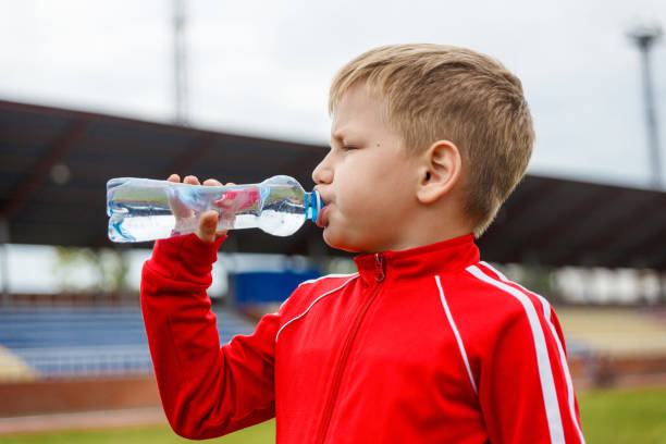 istock boy in a red uniform drinking water from a small bottle at a sports stadium 1147465876