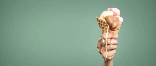 Ice cream in a cone held by a hand is dripping as it melts away.  Panoramic version with a lot of copy space.