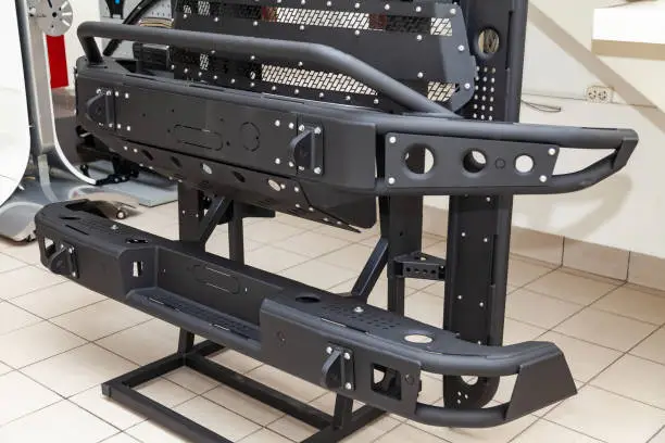 Photo of Stand for demonstration of car body elements reinforced for off-road and made of metal, such as bumper, steps and black grille in the workshop for the installation and tuning of SUV vehicles.