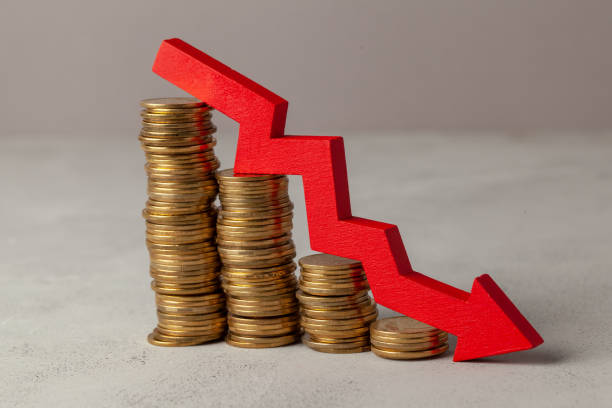 istock Green arrow down over stack of coins by ladder on gray background. 1147472020