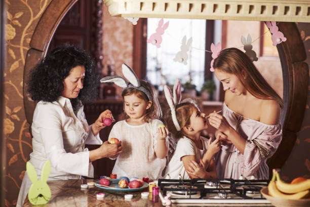 istock Front view. Have happy easter. Two little girls learning by parents how to paint eggs at the holidays 1147475441