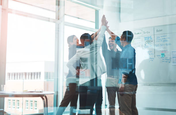 Business is winning when we stick together Shot of a group of young businesspeople joining hands in solidarity in a modern office high five stock pictures, royalty-free photos & images