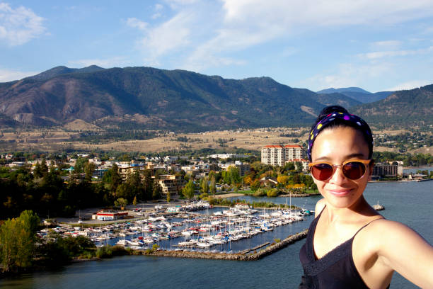 One young adult woman taking a selfie at the view of the City of Penticton, overlooking Okanagan Lake, British Columbia, Canada from Munson Mountain on holiday travel vacation freedom lifestyle.
