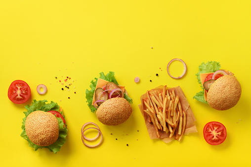 Fast food banner. Juicy meat burgers with beef, tomato, cheese, onion, cucumber and lettuce on yellow background. Top view, copy space. Take away meal. Unhealthy diet concept.