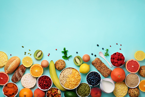 Healthy breakfast ingredients, food frame. Oat and corn flakes, eggs, nuts, fruits, berries, toast, milk, yogurt, orange, banana, peach on blue background. Top view, copy space. Flat lay.